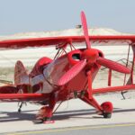 A striking red vintage biplane is parked on a sunny runway, showcasing its bright color and classic design.