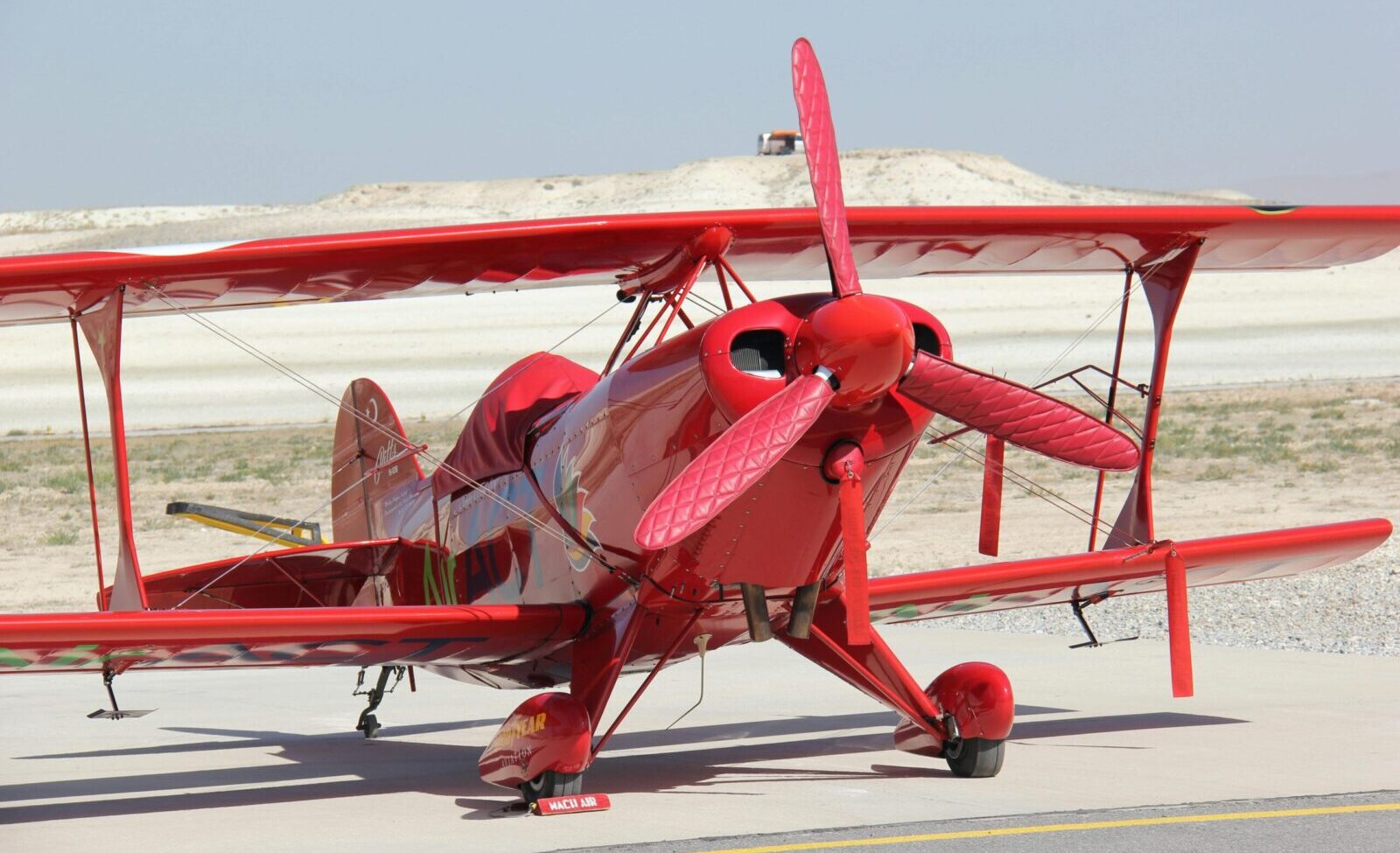 A striking red vintage biplane is parked on a sunny runway, showcasing its bright color and classic design.