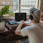Music producer with headphones creating tracks on a laptop in a bright, indoor setting.