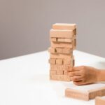 A hand stacks wooden Jenga blocks with words like depression and kindness.