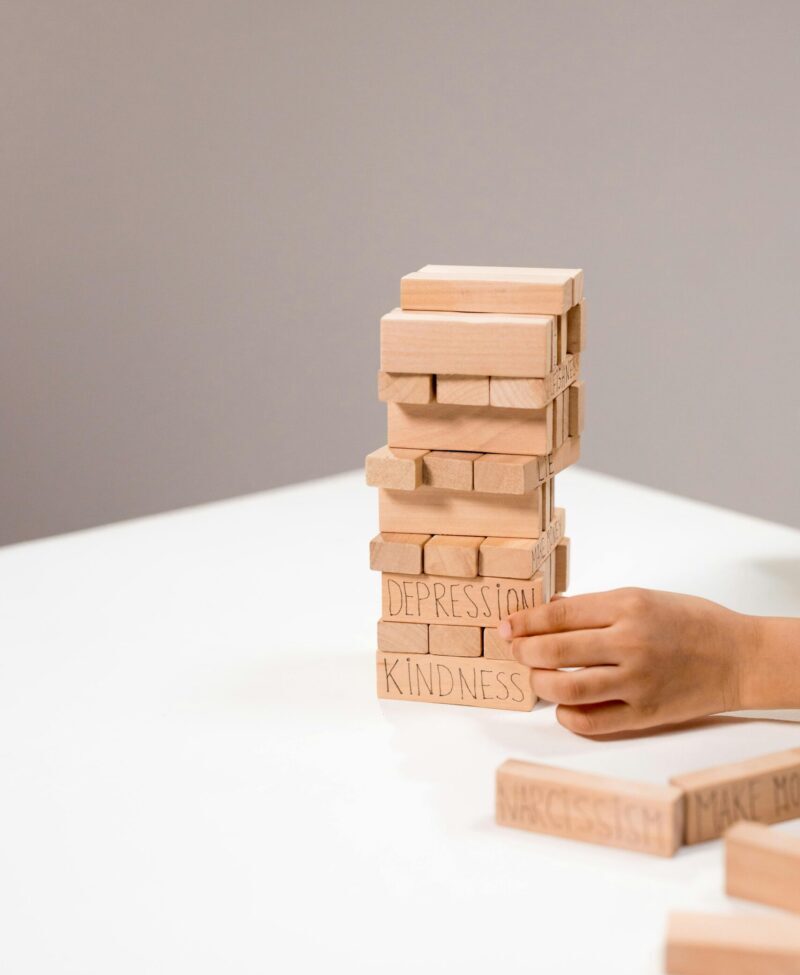 A hand stacks wooden Jenga blocks with words like depression and kindness.